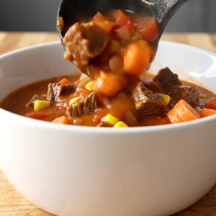 A white shallow bowl filled with beef Mulligan stew featuring tender beef cubes, potatoes, carrots