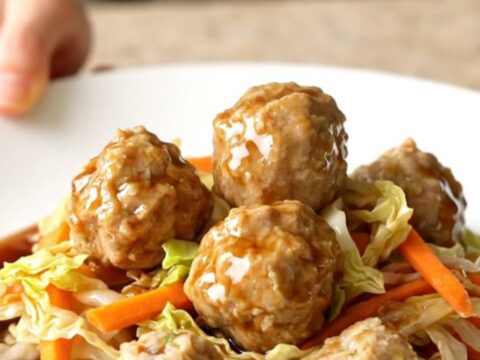 A high-angle shot of a slow cooker filled with chicken meatballs and shredded cabbage.