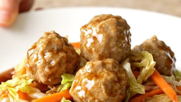 A high-angle shot of a slow cooker filled with chicken meatballs and shredded cabbage.