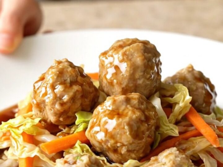 A high-angle shot of a slow cooker filled with chicken meatballs and shredded cabbage.