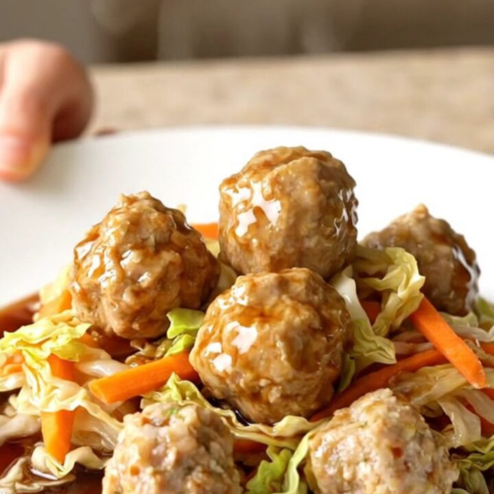 A high-angle shot of a slow cooker filled with chicken meatballs and shredded cabbage.