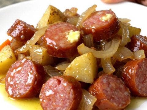 A close-up view of the slow cooker filled with sliced smoked sausage, cubed potatoes, carrots, and onions.