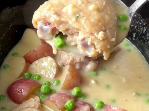 A slow cooker filled with tender chicken thighs, red potatoes, and peas in a rich, creamy white sauce.