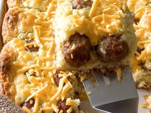 A golden, puffed breakfast casserole in a ceramic dish, featuring sausage meatballs and melted cheddar cheese.
