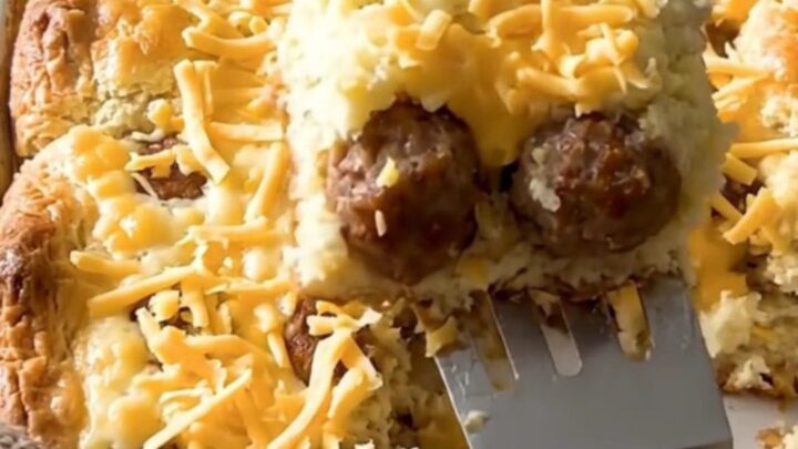 A golden, puffed breakfast casserole in a ceramic dish, featuring sausage meatballs and melted cheddar cheese.