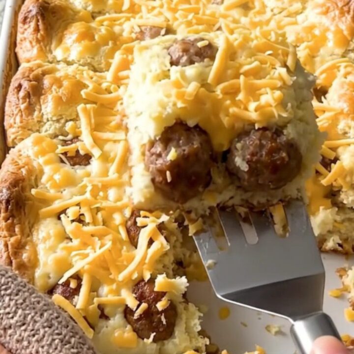 A golden, puffed breakfast casserole in a ceramic dish, featuring sausage meatballs and melted cheddar cheese.