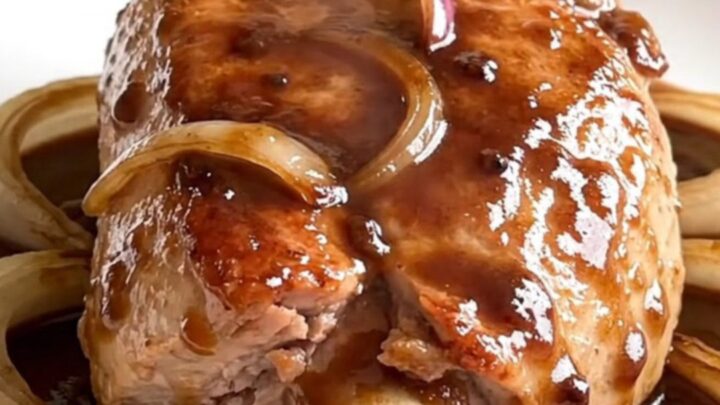 A finished slow cooker pork tenderloin sliced on a white plate with onions and red wine gravy.