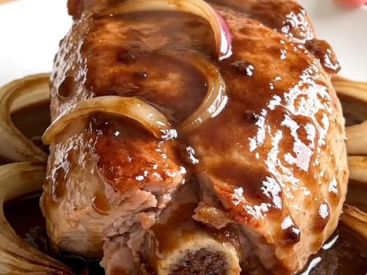 A finished slow cooker pork tenderloin sliced on a white plate with onions and red wine gravy.