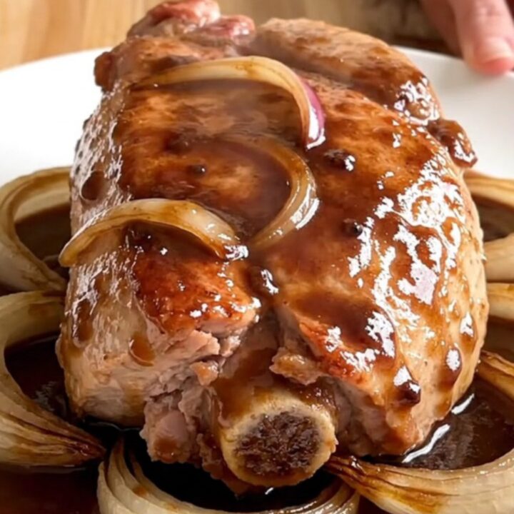 A finished slow cooker pork tenderloin sliced on a white plate with onions and red wine gravy.
