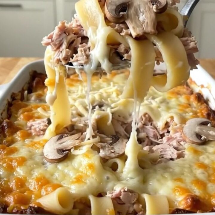 A top-down view of a golden, bubbling Mushroom Swiss Turkey Noodle Bake in a white ceramic dish.