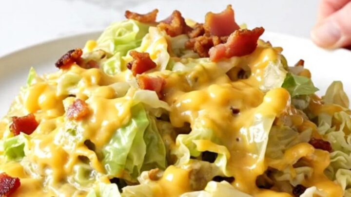 A close-up of a slow cooker filled with chopped cabbage, bacon, and melted cheddar cheese.