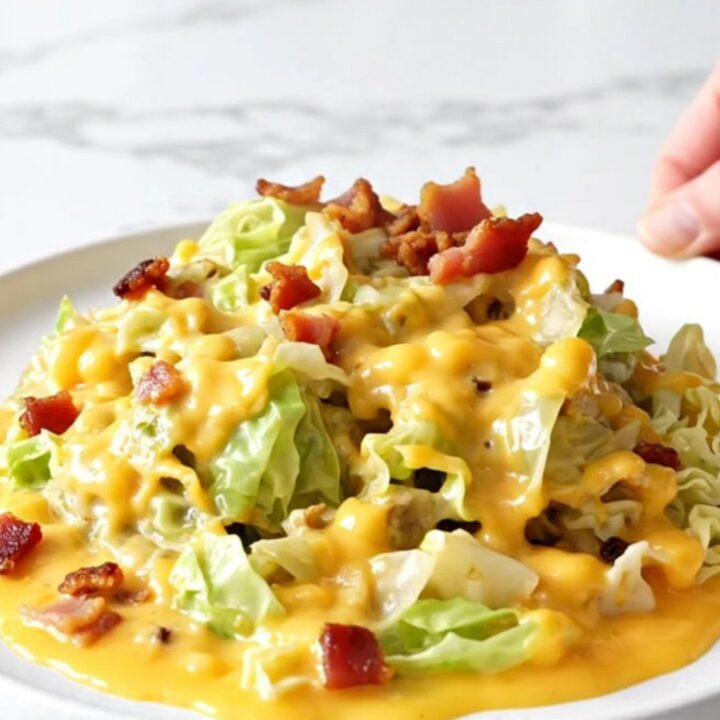 A close-up of a slow cooker filled with chopped cabbage, bacon, and melted cheddar cheese.