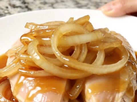 A close-up shot of tender slow-cooked chicken breasts topped with sweet onion slices and sesame seeds.