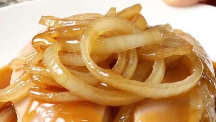 A close-up shot of tender slow-cooked chicken breasts topped with sweet onion slices and sesame seeds.
