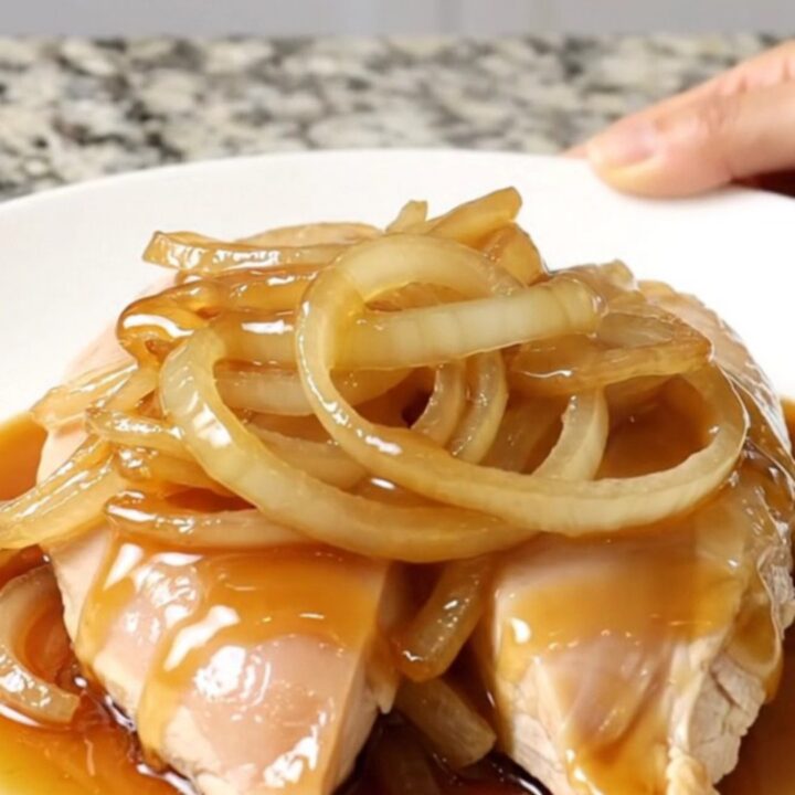 A close-up shot of tender slow-cooked chicken breasts topped with sweet onion slices and sesame seeds.