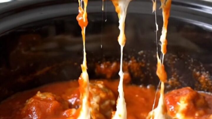 A close-up of tender chicken meatballs coated in thick red marinara sauce and melted mozzarella cheese in a slow cooker.