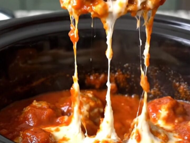 A close-up of tender chicken meatballs coated in thick red marinara sauce and melted mozzarella cheese in a slow cooker.