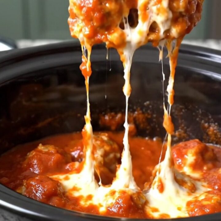 A close-up of tender chicken meatballs coated in thick red marinara sauce and melted mozzarella cheese in a slow cooker.
