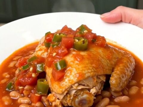 A close-up of tender chicken thighs and pinto beans in a rich tomato sauce served on a white plate.