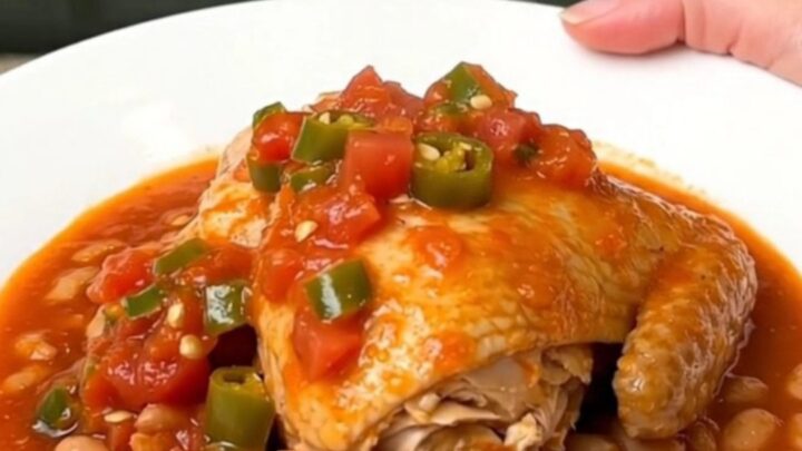 A close-up of tender chicken thighs and pinto beans in a rich tomato sauce served on a white plate.