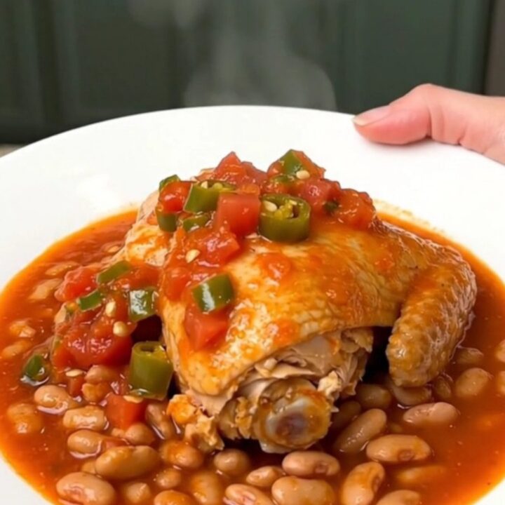 A close-up of tender chicken thighs and pinto beans in a rich tomato sauce served on a white plate.