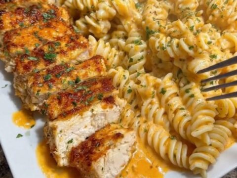 A close-up of steaming, rich cheese-coated rotini pasta with juicy