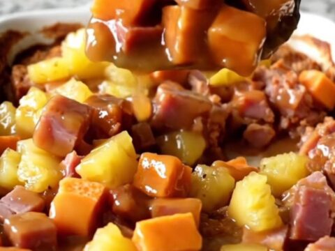 A large ceramic dish filled with cubes of roasted sweet potato, savory ham, and pineapple chunks in a golden glaze.