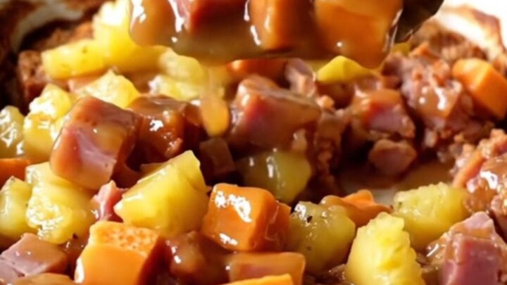 A large ceramic dish filled with cubes of roasted sweet potato, savory ham, and pineapple chunks in a golden glaze.