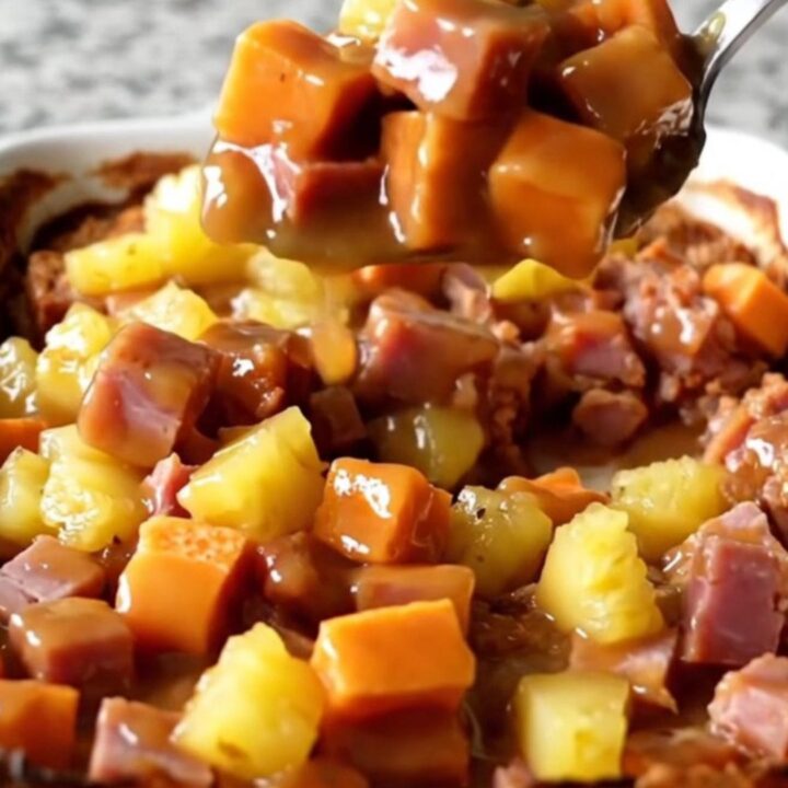 A large ceramic dish filled with cubes of roasted sweet potato, savory ham, and pineapple chunks in a golden glaze.