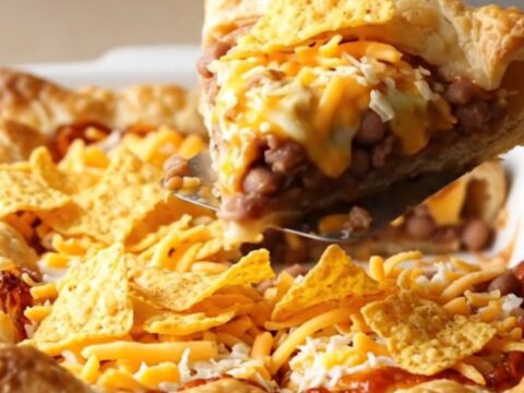 A golden-brown taco pizza crescent bake in a white dish on a beige countertop.