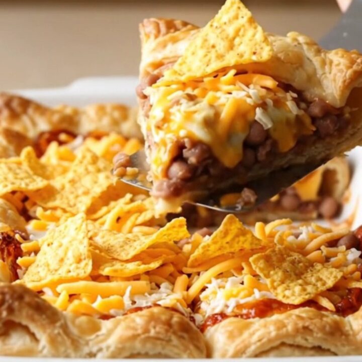 A golden-brown taco pizza crescent bake in a white dish on a beige countertop.