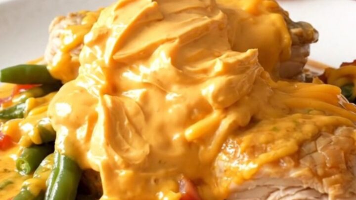 A slow cooker filled with chicken thighs, green beans, bacon, and melted cheddar cheese.