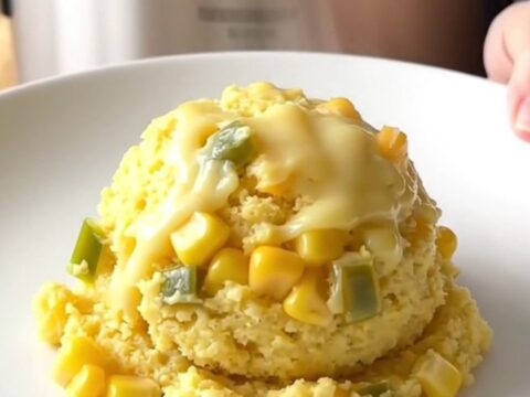 A golden, freshly scooped portion of jalapeno cheddar corn pudding on a white plate.