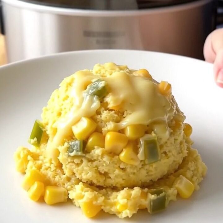 A golden, freshly scooped portion of jalapeno cheddar corn pudding on a white plate.