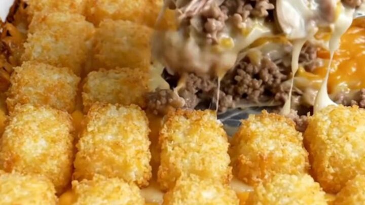 A golden-brown potato tot casserole in a white ceramic dish on a speckled countertop.