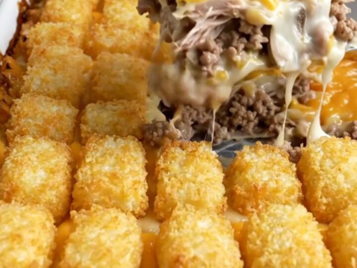 A golden-brown potato tot casserole in a white ceramic dish on a speckled countertop.
