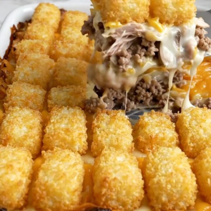 A golden-brown potato tot casserole in a white ceramic dish on a speckled countertop.