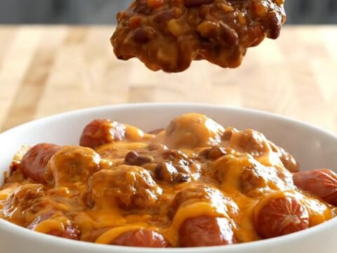 A close-up of a slow cooker filled with mini sausages covered in a thick, melty orange chili cheese sauce.