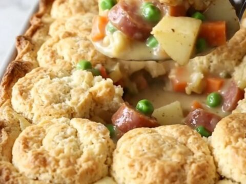 A rustic 9x13 inch baking dish filled with a creamy smoked sausage, potato, and vegetable bake topped with golden biscuits.