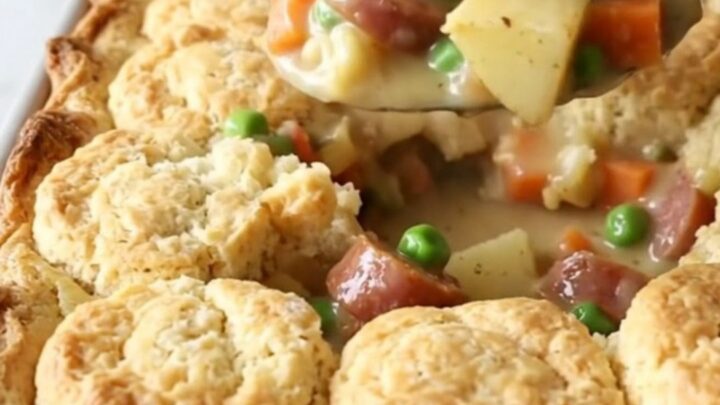 A rustic 9x13 inch baking dish filled with a creamy smoked sausage, potato, and vegetable bake topped with golden biscuits.