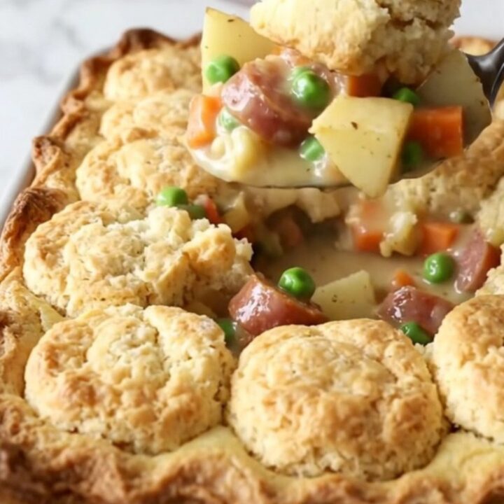 A rustic 9x13 inch baking dish filled with a creamy smoked sausage, potato, and vegetable bake topped with golden biscuits.