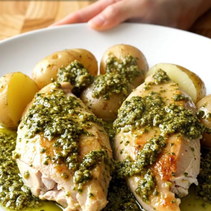 A slow cooker filled with tender chicken breasts and golden baby potatoes coated in a thick, vibrant green pesto sauce.