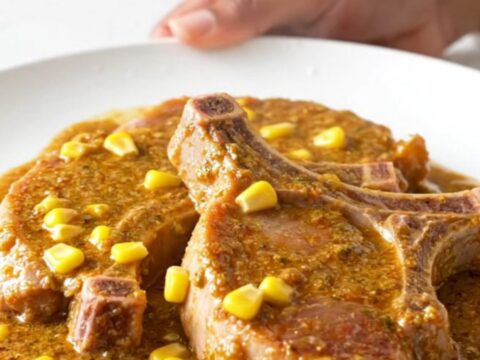 Creamy slow-cooked pork chops covered in a rich corn and chili sauce on a white plate.