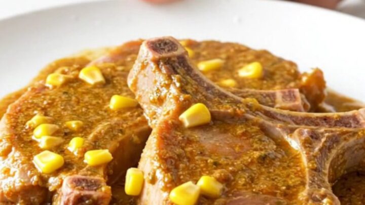 Creamy slow-cooked pork chops covered in a rich corn and chili sauce on a white plate.