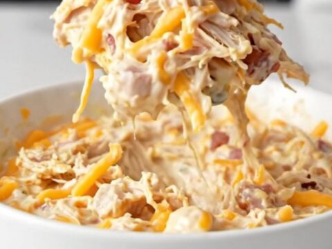 A close-up of a creamy chicken bacon ranch dip in a black slow cooker, featuring melted cheese and visible bacon bits.