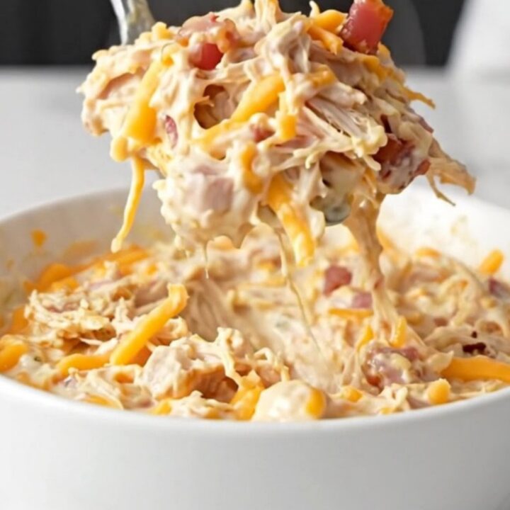 A close-up of a creamy chicken bacon ranch dip in a black slow cooker, featuring melted cheese and visible bacon bits.