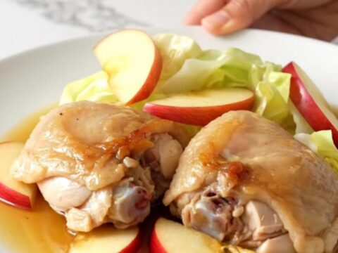 A top-down view of a black slow cooker filled with chicken thighs, cabbage wedges, and apple slices.
