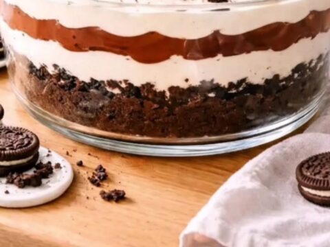 A clear glass trifle bowl filled with distinct layers of white cream and dark chocolate pudding topped with cookie crumbs.