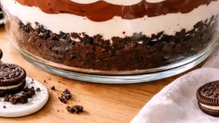 A clear glass trifle bowl filled with distinct layers of white cream and dark chocolate pudding topped with cookie crumbs.