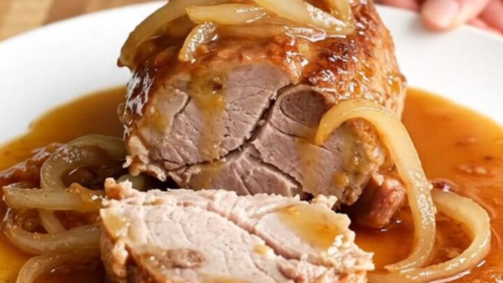 Slow cooker honey chipotle pork tenderloin with sliced onions and a glossy glaze on a white plate.